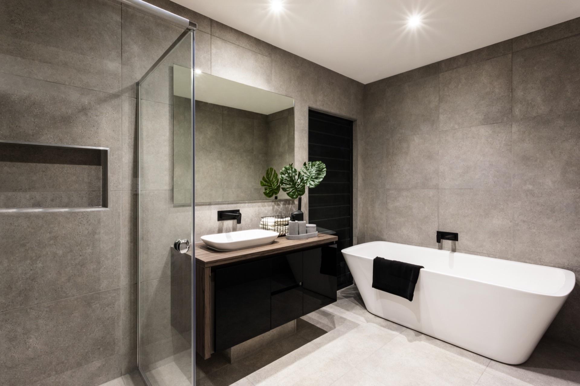 Modernes Badezimmer mit großformatigen grauen Wand- und Bodenfliesen, freistehender Badewanne, schwarzer Waschtischzeile und Glasdusche