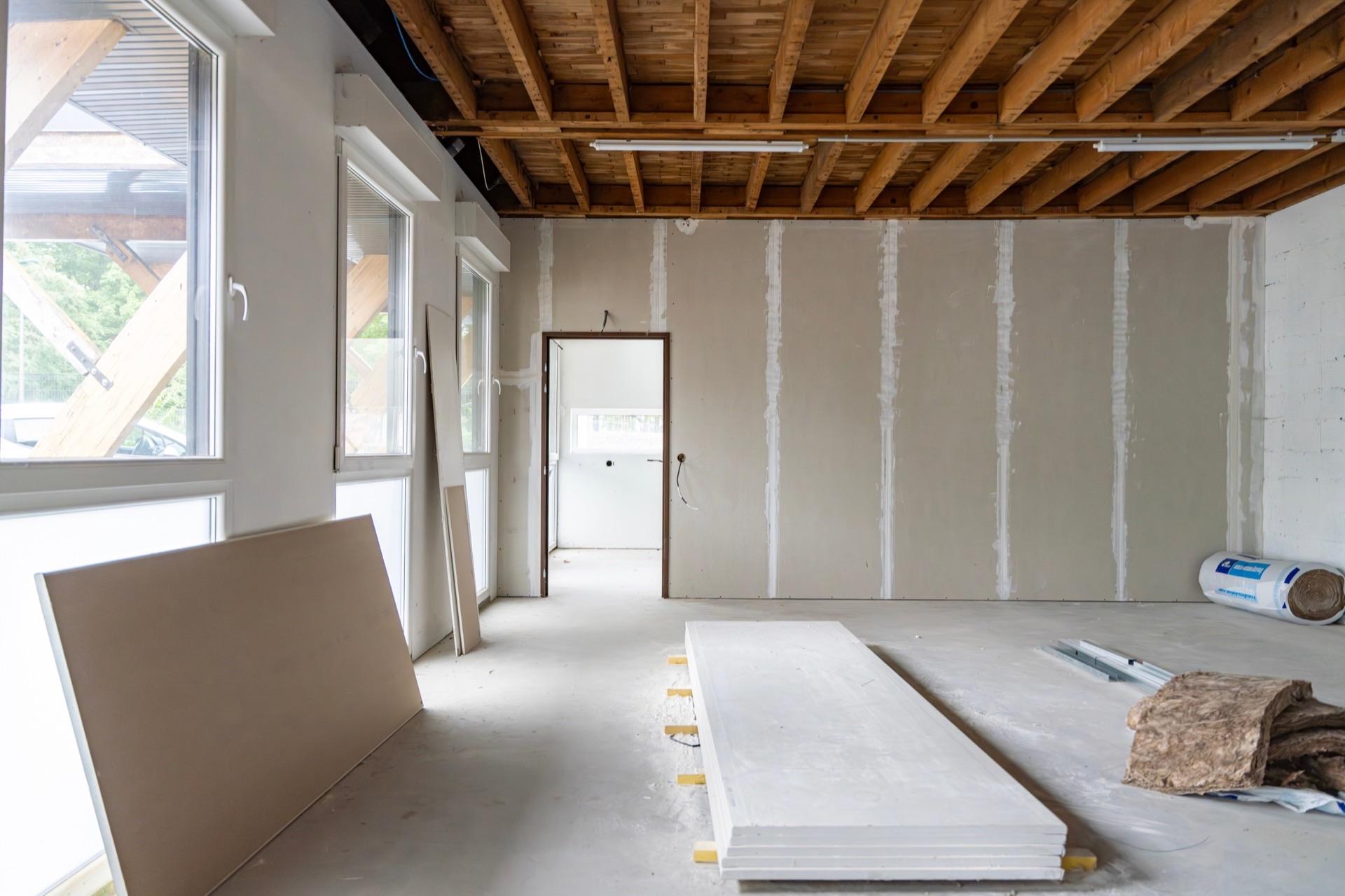 Renovierraum im Rohbau mit Trockenbauwänden, Deckenständern und Baumaterialien auf Betonboden