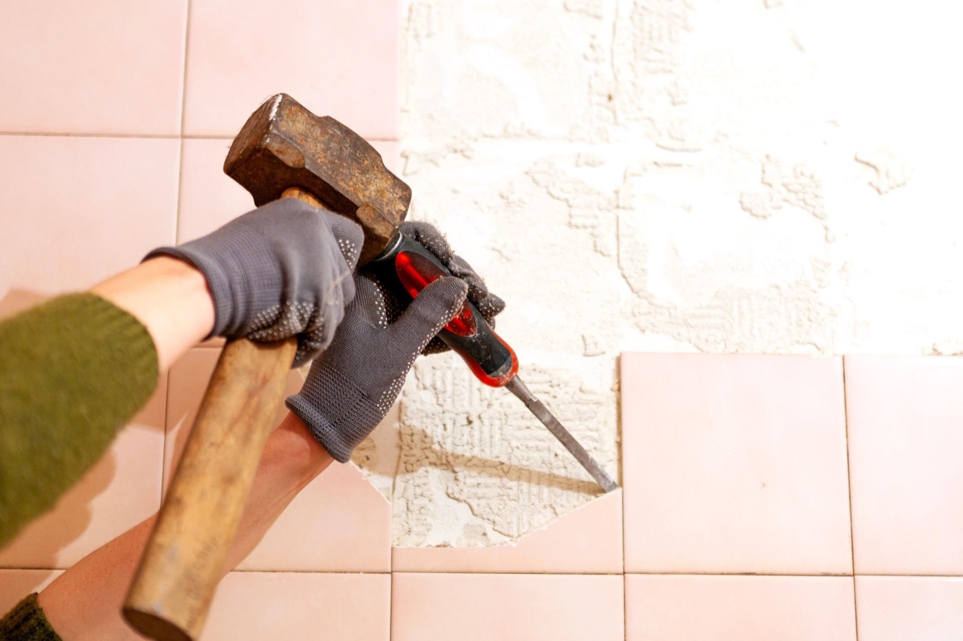 Handwerker entfernt beige Fliese mit Hammer und Meißel